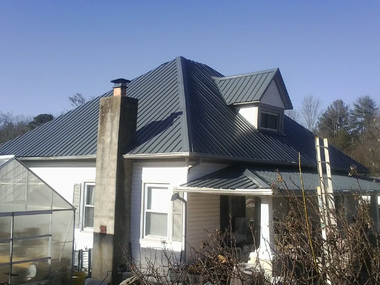 Dark blue standing seam metal roof on a white farmhouse with dormer — Slate & Tile Roof Repair by Roofing Brothers in Roslindale