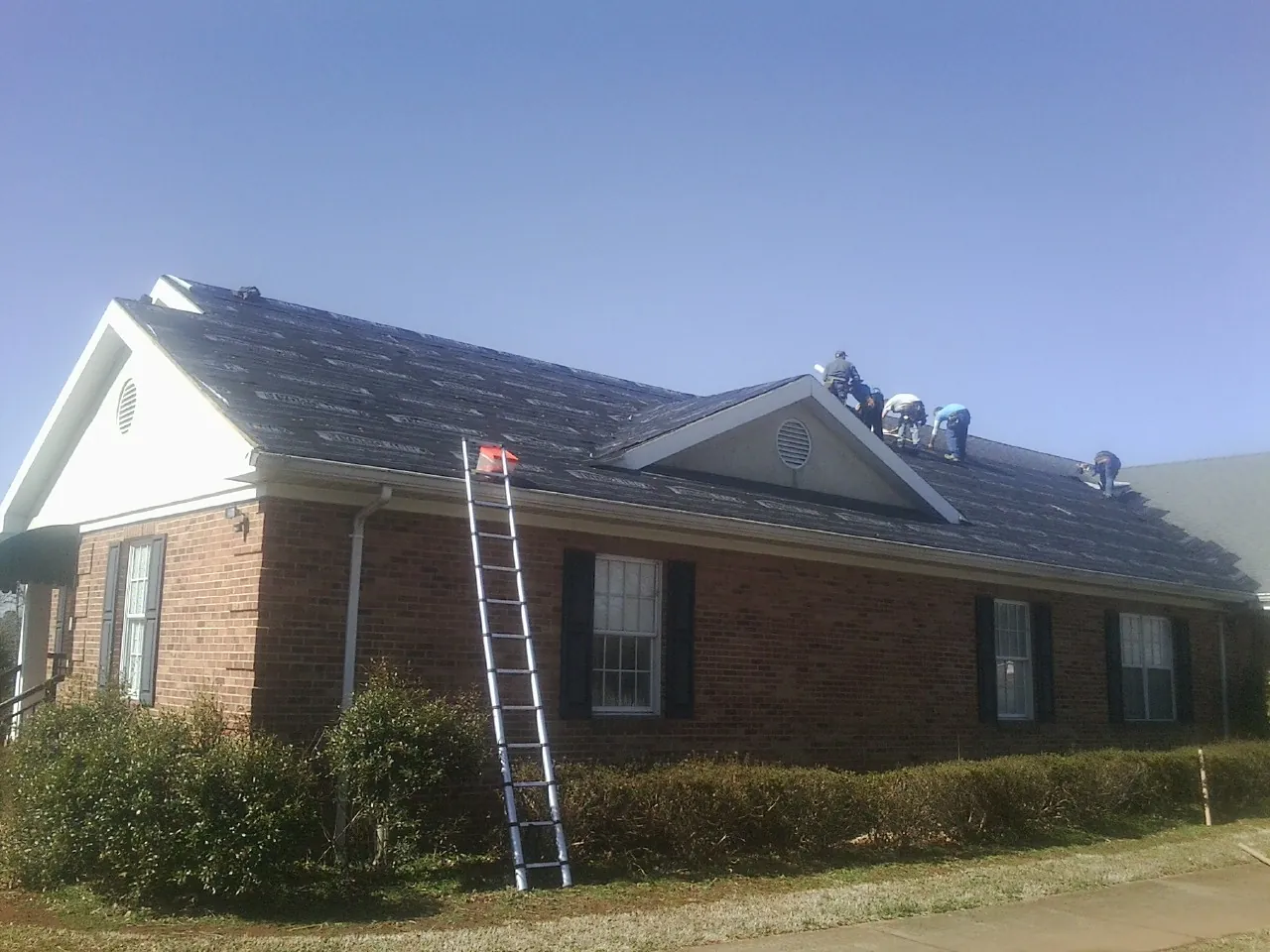 Crew tearing shingles off a brick ranch roof with a ladder set — Emergency Roof Repair work by our crew in Roslindale