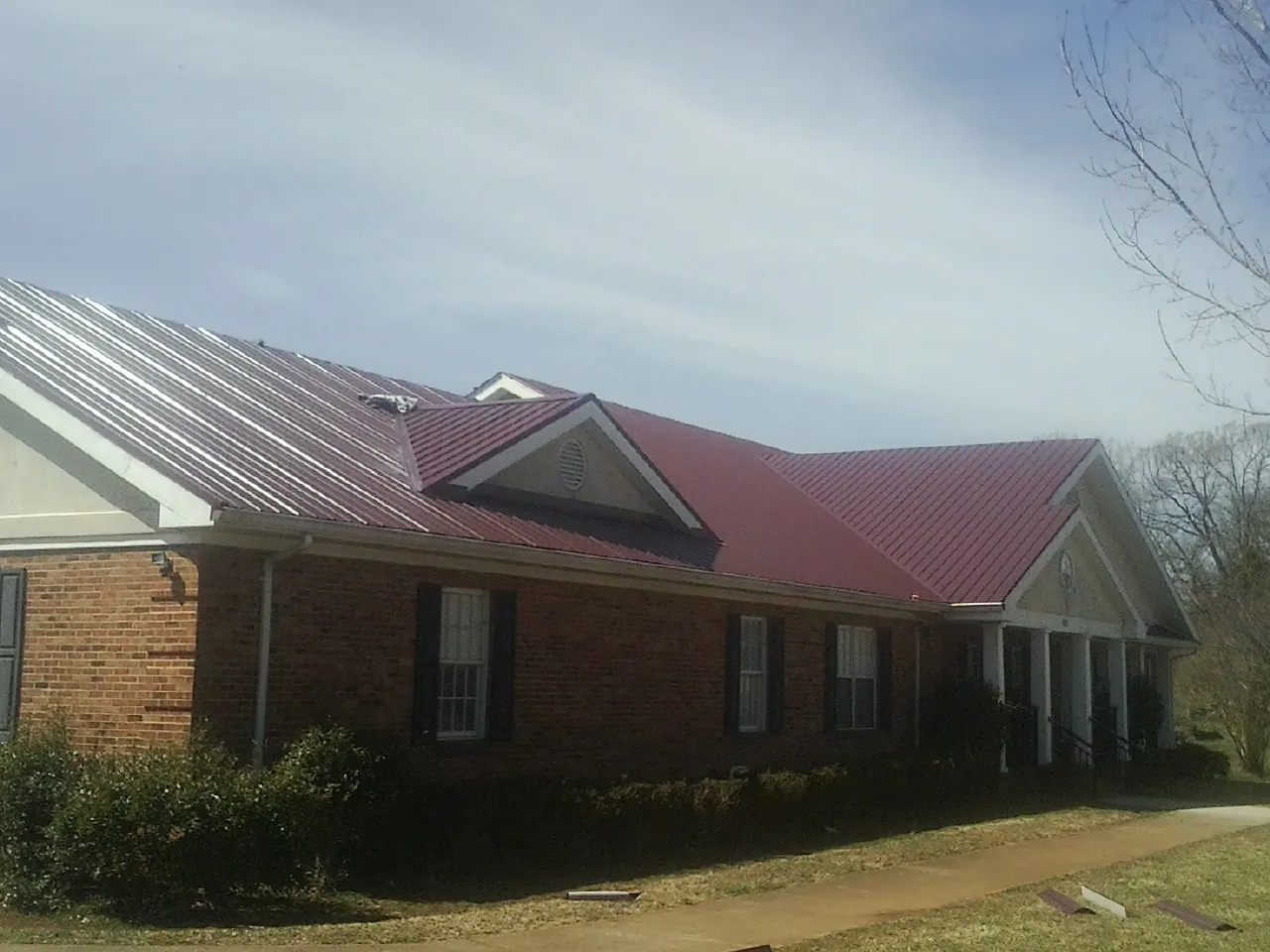 Red metal roof with gabled entries on a long brick building, from a Hail Damage Roof Repair job in Roslindale