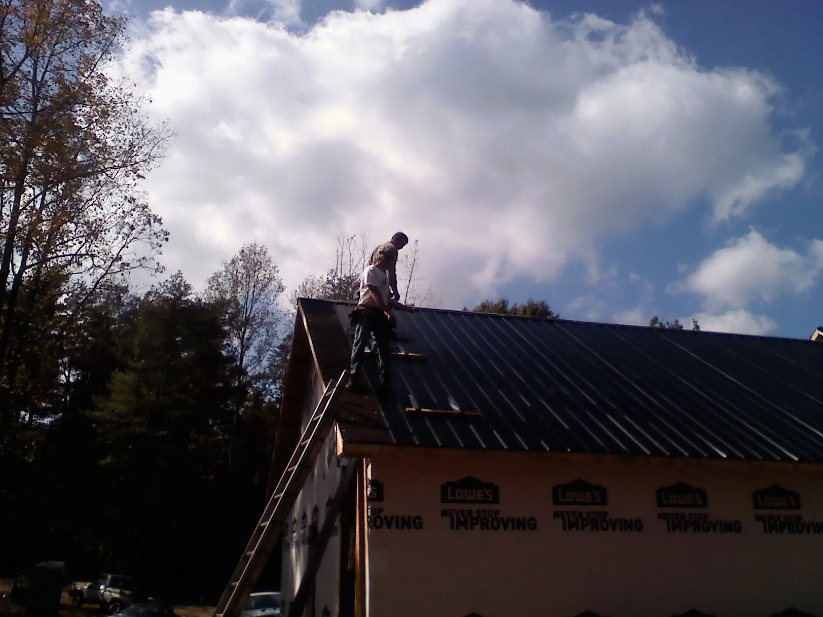 Roofer fastening dark metal panels high against a cloudy sky, from a Roof Inspection job in Roslindale