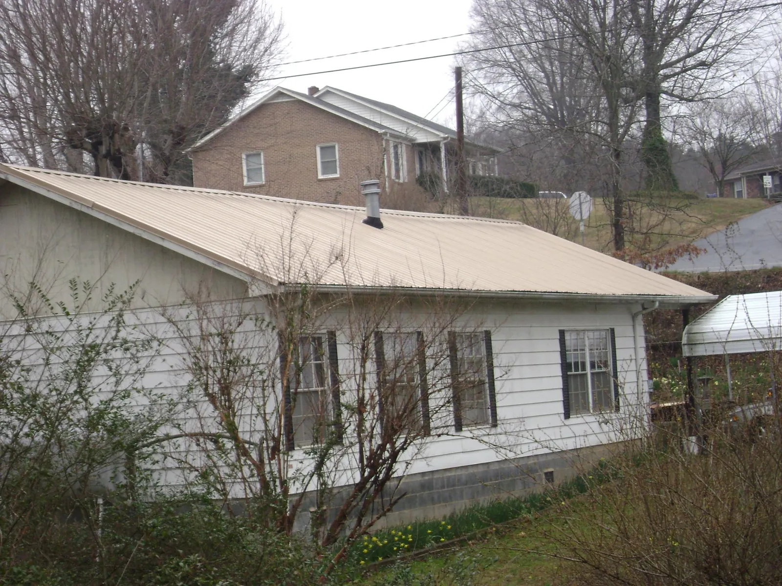 Tan metal roof on a white sided house set into a hillside — Commercial Roofing by Roofing Brothers in Roslindale